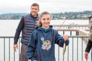 Smiling girl holding fish on dock with man